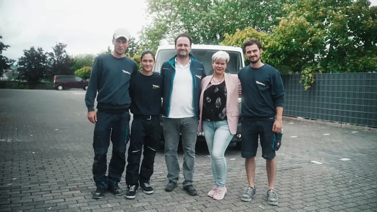 Fünf Personen des Betriebs stehen nebeneinander vor dem Firmenwagen